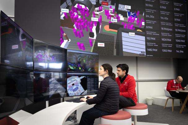 Eduardo de la Espriella in the red Outsight hoodie at the Outsight MWC booth, colleague working at a terminal, SHIFT dashboards on the back wall